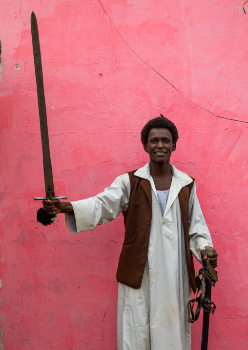 Beja tribe warrior with his sword in front of a pink wall, Red Sea State, Port Sudan, Sudan