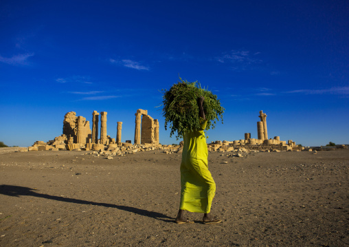 Sudan, Nubia, Soleb, woman carrying grass passing in front of the big soleb temple