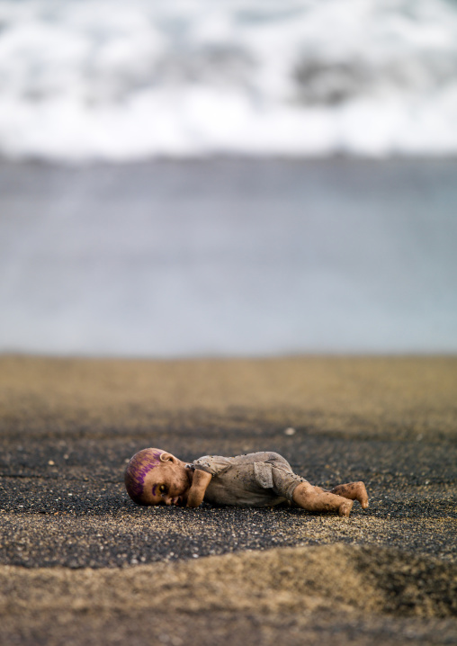 Doll lying on black sandy beach at waterside, Shefa Province, Efate island, Vanuatu