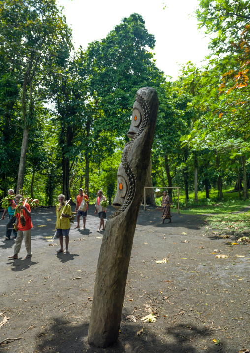 Men coming back from bananas harvesting passing in front of a slit gong drum, Malampa Province, Ambrym island, Vanuatu