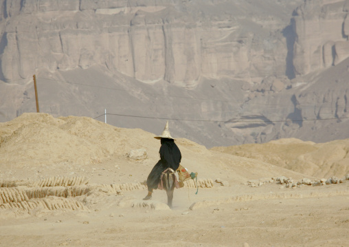 Hadramaut Woman With  A Tall Cone Hat Riding A Donkey In The Dust, Yemen