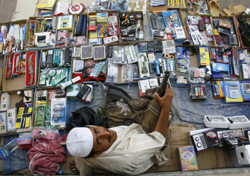 Seller Holding A Gun And Sitting Among The Items For Sale, Tarim Market, Yemen